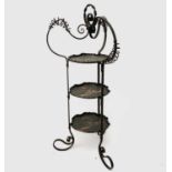 An Arts and Crafts wrought iron cake stand, fitted with three copper trays, each embossed with