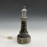 A Cornish serpentine table lamp, modelled as a lighthouse on a rocky base. Height 34cm.