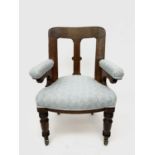 A Victorian oak framed desk chair, with upholstered back and seat and padded arms, on turned front