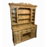 A pine dresser, the rack with four shelves flanked by a pair of glazed cupboard doors, the lower