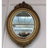 An oval gilt wall mirror, 19th century, with ivy and berry cresting and mount, with a deep moulded