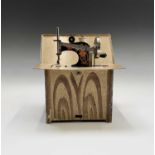 A Swedish tinplate and painted toy 'sewing machine', circa 1920, contained in a faux bois cabinet,