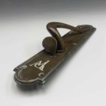 A decorative bronze door handle, circa 1910, with scrolled handle and white enamel initials PW,