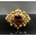A Victorian carbuncle brooch set ornately in gold with flowers in relief and 'c' scrolls 42mm 8.6g.