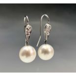 A pair of 10.3mm pearl drop earrings each hangs from a diamond set pear shape link, 4g.