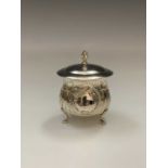 An Edwardian silver tea caddy or lidded sugar on three feet beneath spiral fluting and a repousse