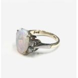 An 18ct gold ring, set an oval opal measuring 12.3x9.7mm to each side a pair of diamonds.