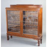 An Edwardian Art Nouveau mahogany bookcase with raised back, fitted shelves enclosed by lead