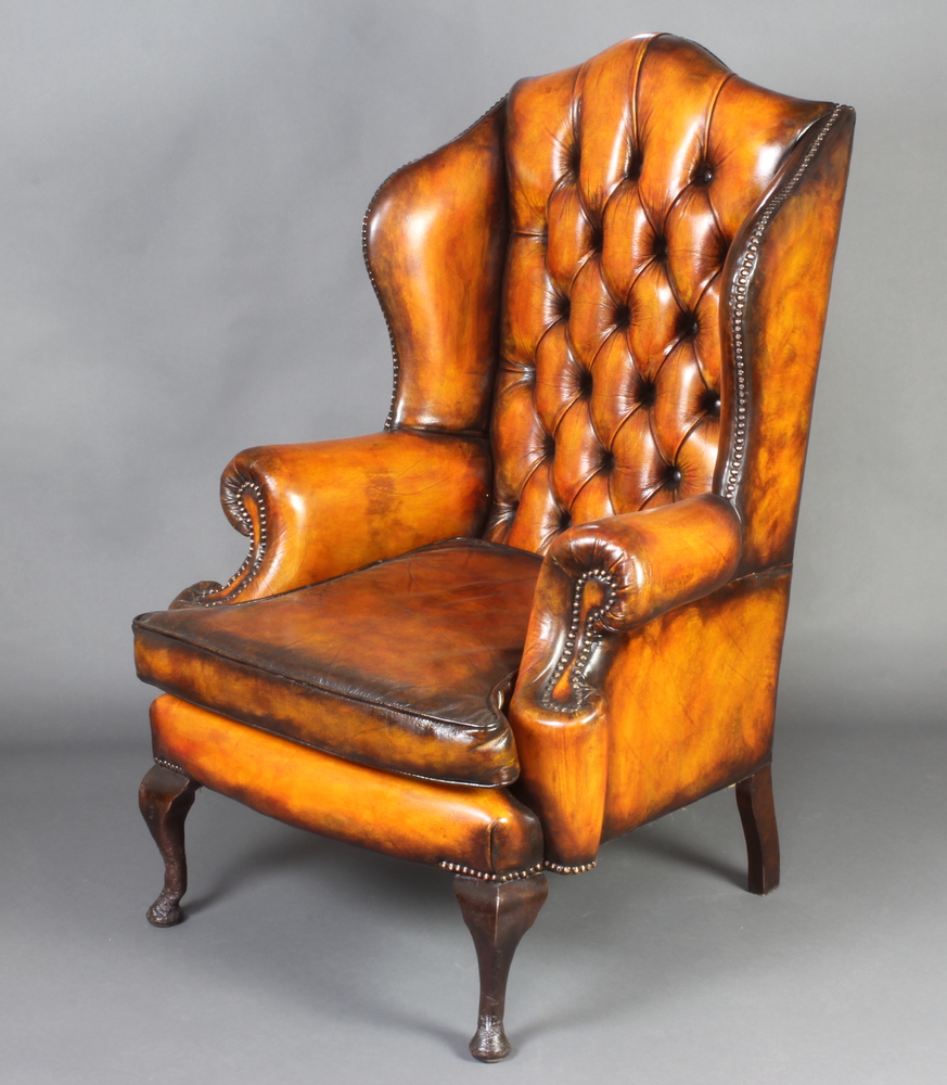 A Georgian style winged armchair upholstered in brown buttoned leather, raised on cabriole