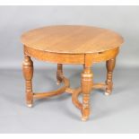 An Edwardian light oak extending dining table with 1 extra leaf, raised on cup and cover supports