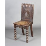 A Victorian carved oak hall chair with solid seat and carved panel back, raised on bobbin turned