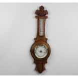 An aneroid barometer and thermometer with porcelain dial contained in a carved oak wheel case