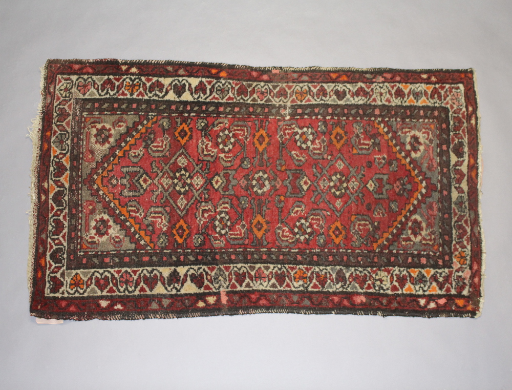 A red and tan ground Persian rug with 2 stylised diamonds to the centre 123cm x 72cm Some old moth