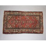 A red and tan ground Persian rug with 2 stylised diamonds to the centre 123cm x 72cm Some old moth