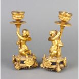 A pair of 19th/20th Century gilt ormolu candlesticks supported by figures of cherubs 18cm h