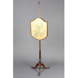 An Edwardian shield shaped pole screen raised on a turned mahogany column and tripod base with