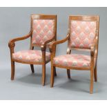 A pair of mahogany Empire style open arm chairs upholstered in floral material, raised on outswept