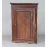 A Georgian oak hanging corner cabinet with moulded and dentil cornice, fitted shelves enclosed by