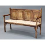 A bleached oak settle of panelled construction, having an upholstered seat and raised on square