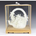 A Chinese porcelain model of a floral encrusted teapot, contained in an light oak display cabinet