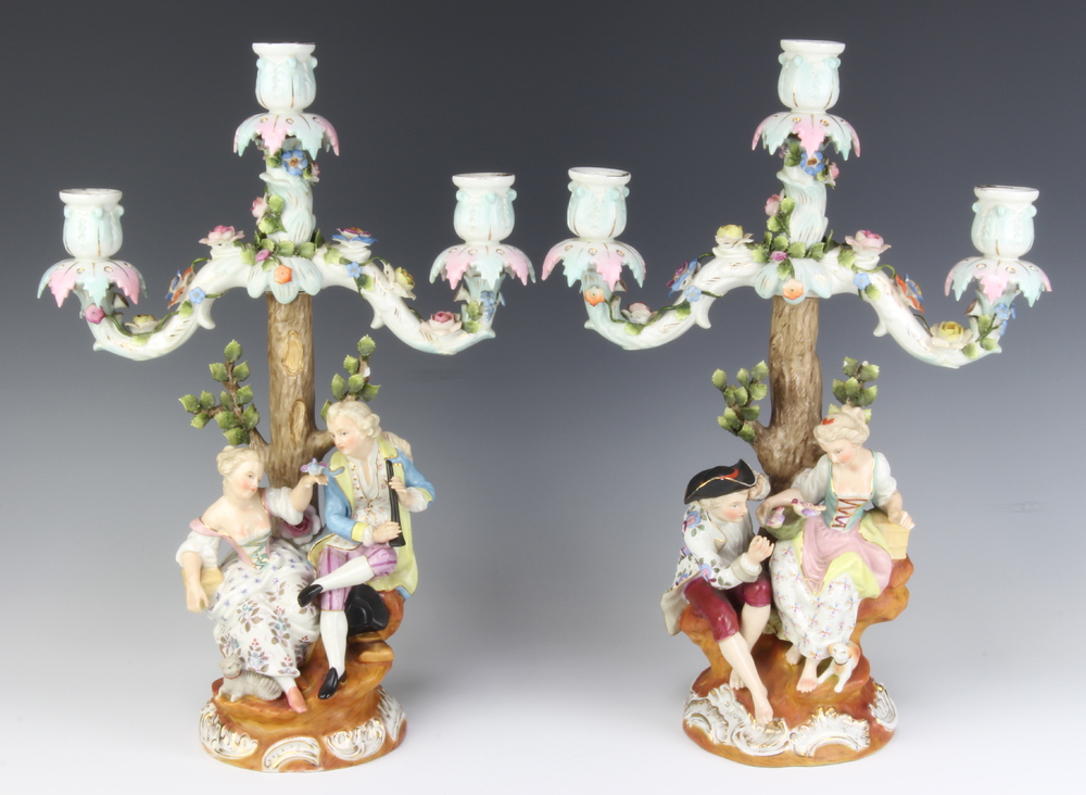 A pair of Sitzendorf 3 light candelabra decorated with figures beneath trees, raised on rococo bases