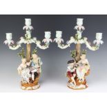 A pair of Sitzendorf 3 light candelabra decorated with figures beneath trees, raised on rococo bases