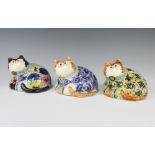 Three Rye Cinque Port Pottery figures of reclining cats with glass eyes, all decorated with