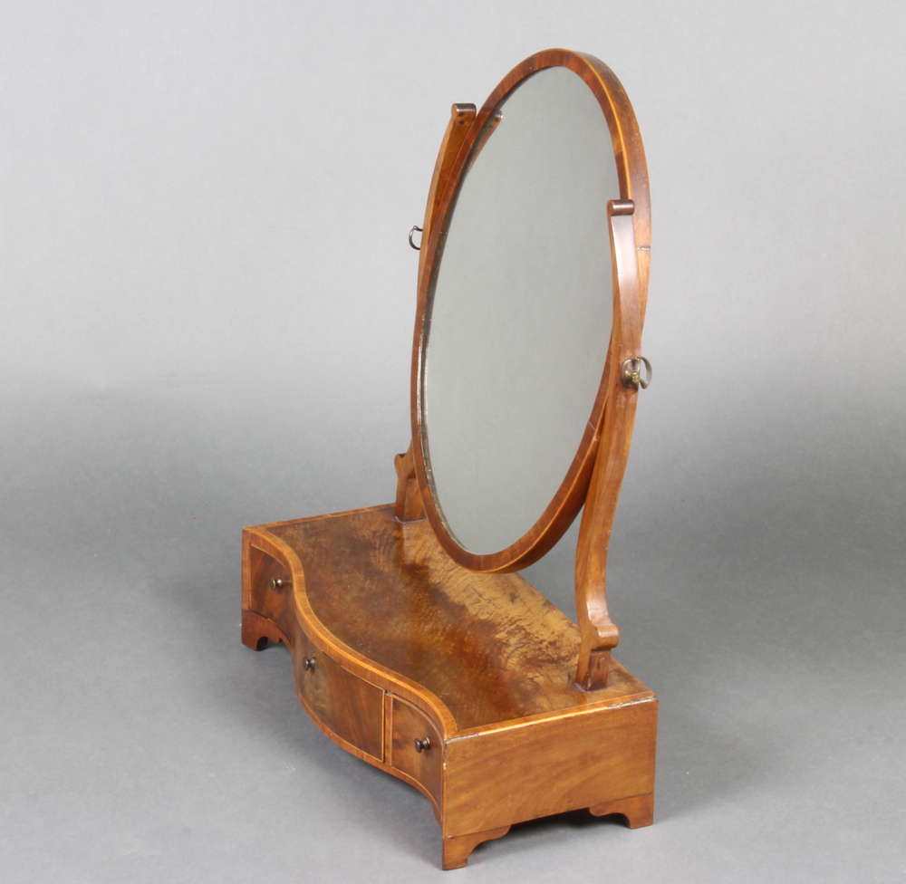 A Sheraton style oval plate dressing table mirror contained in a mahogany frame and raised on