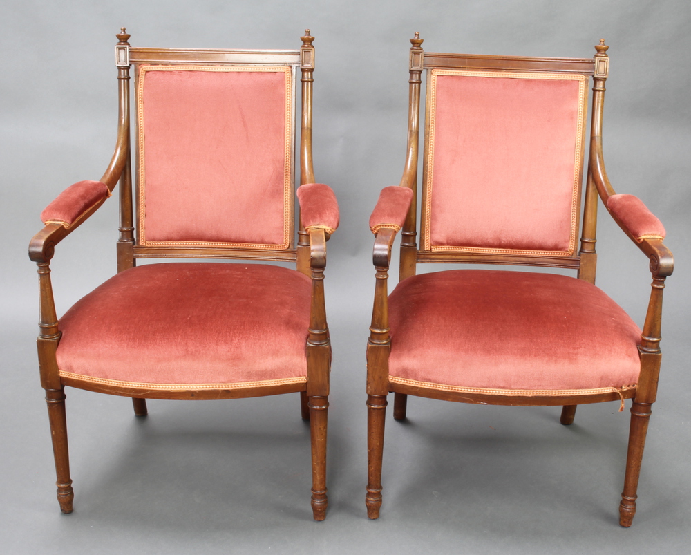 A pair of French Empire style walnut open arm chairs raised on turned supports, the seats and