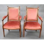 A pair of French Empire style walnut open arm chairs raised on turned supports, the seats and