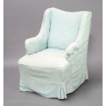 An Edwardian winged armchair with blue loose cover, raised on turned supports