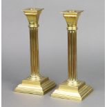 A pair of brass reeded candlesticks with detachable sconces raised on square stepped bases 24cm h