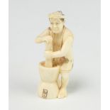 A Japanese ivory Meiji period Netsuke in the form of a standing man grinding flour in a double ended
