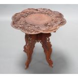 A circular Burmese carved hardwood occasional table decorated dragons, raised on a folding base 55cm