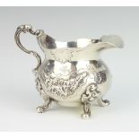 A Victorian repousse silver cream jug decorated with flowers and grapes on scroll feet London