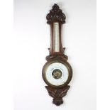 An Edwardian aneroid barometer and thermometer with paper dial contained in a carved oak wheel