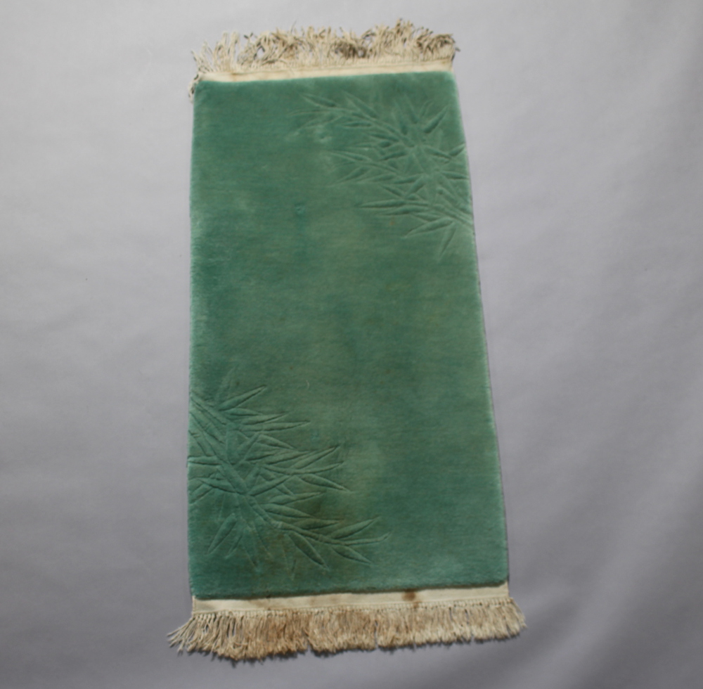 A sculpted green ground Chinese rug with blue decoration 129cm x 64cm Some staining
