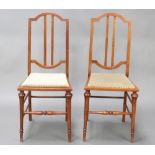 A pair of Edwardian mahogany stick and rail back bedroom chairs with upholstered seats, raised on