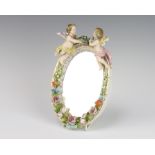 A German porcelain oval dressing table mirror decorated with flowers and surmounted by 2 angels with