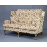 A Queen Anne style wing back 2 seat sofa upholstered in tapestry material, raised on cabriole