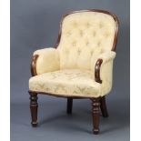 A Victorian mahogany show frame armchair upholstered in yellow buttoned material, raised on turned