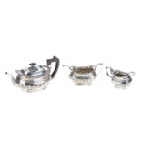 AN EDWARDIAN SILVER THREE PIECE TEA SET of compressed fluted form on ball feet, comprising:- Teapot,