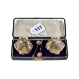 A PAIR OF EDWARDIAN SILVER SHELL FORM SALT CELLARS on ball feet and matching spoons, maker:- WA,
