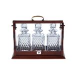 A SET OF THREE SQUARE CUT-GLASS DECANTERS AND STOPPERS with mahogany tantalus frame.