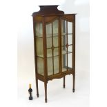 An Edwardian mahogany display cabinet with a shaped upstand above a glazed door with marquetry