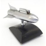 A 20thC novelty space rocket tabletop lighter raised on a wooden base. Approx. 3 3/4" high.