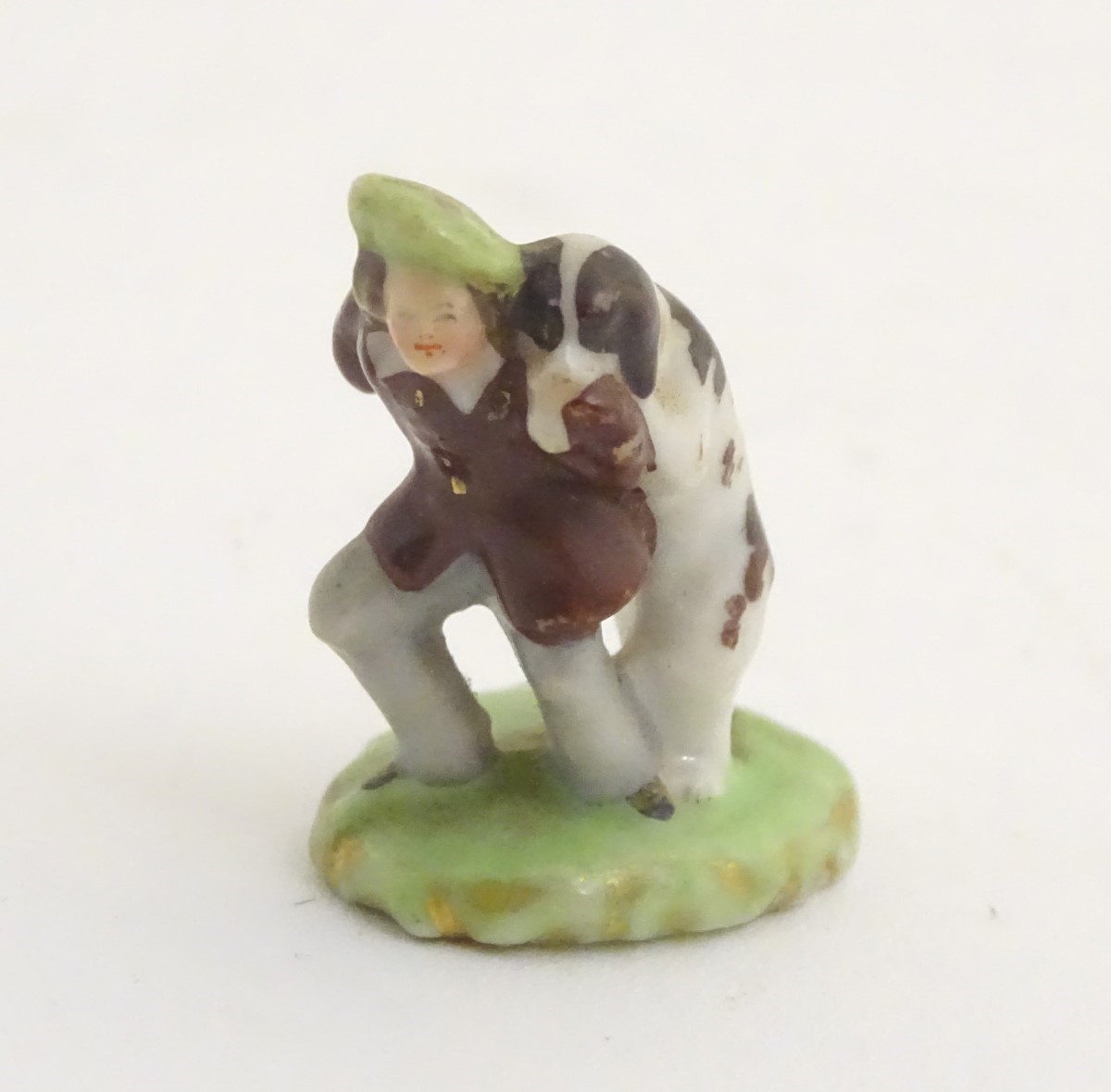 A miniature Rockingham style figure of a man wearing a tam-o-shanter with a dog on an oval base.