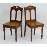 A pair of early 20thC oak hall chairs with broken pediments above chamfered frames and pierced
