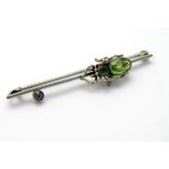 A white metal bar brooch set with spider to centre set with green stones. 2 ¼" long.