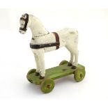 A 19thC folk art carved and painted pull along horse toy on a green painted platform with wooden